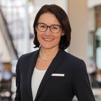 Portrait of a smiling businesswoman wearing glasses and a pearl necklace.