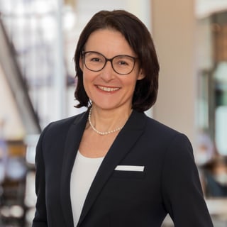 Porträt einer lächelnden Geschäftsfrau mit Brille und Perlenkette.