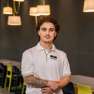 Kellner in Restaurant mit weissen Hemd und Schürze, leere Tische im Hintergrund.