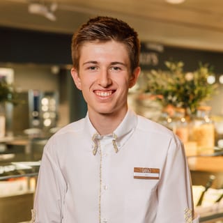 Junger Mann in weissem Hemd in einem Geschäft oder Café stehend.