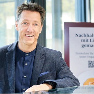 Mann lächelt neben Schild über Nachhaltigkeit.