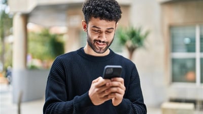 Lächelnder Mann schaut auf sein Handy im Freien.