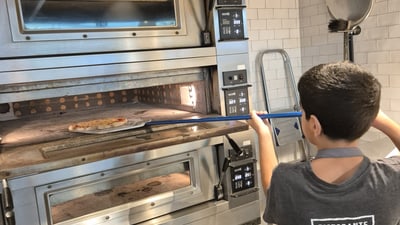 Kind backt Pizza in Ofen einer Pizzeria-Küche.