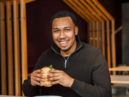 Lächelnder Mann hält einen Burger, sitzt in einem Restaurant.