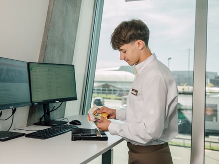 Mann in Uniform zählt Geldscheine am Schreibtisch mit zwei Monitoren.
