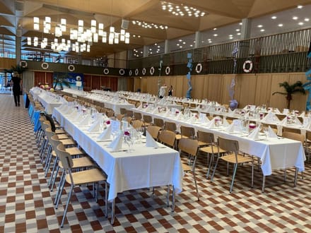 Festlich gedeckter Saal mit langen Tischreihen und Stühlen.