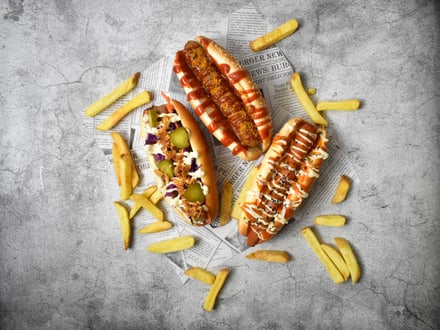 Drei Hotdogs mit Pommes auf Zeitungspapier.