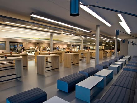 Moderne Cafeteria mit langen Tischen und Bänken.