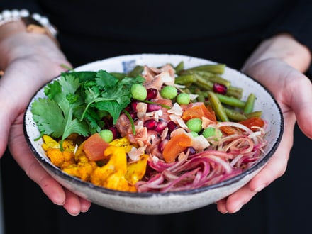 Eine Frau hält eine Bowl mit gesunden und frischen Zutaten in den Händen.