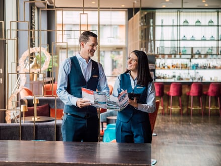 Zwei Hotelmitarbeiter in Uniform stehen in der Lobby und halten Broschüren.