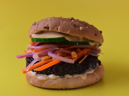 Vegetarischer Burger mit Gemüse auf gelbem Hintergrund.