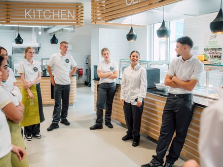 Küchenmitarbeiter stehen im Kreis in einer Kantine zusammen.",