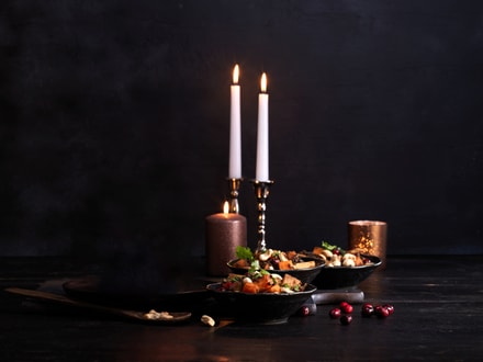 Stimmungsvolles Abendessen bei Kerzenlicht mit zwei brennenden Kerzen und Essen in Pfannen auf dunklem Hintergrund.