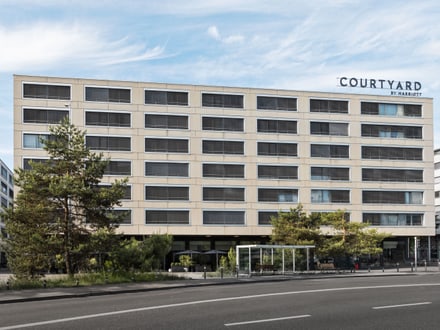Fassade eines Courtyard-Hotels mit Bäumen davor.