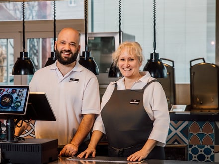 Zwei Personen stehen an einem Restauranttresen mit Kasse.