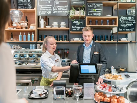 Kundenbedienung in einem modernen Café mit Theke und Kreidetafel-Menü.