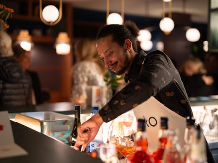 Barkeeper mischt Getränke an einer Bar mit Flaschen im Vordergrund.