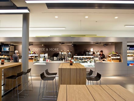 Moderne Cafeteria mit Theke und hohen Tischen.