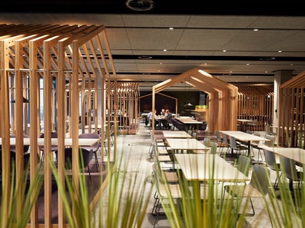 Stylisches und modernes Restaurant mit vielen Tischen und durch Holzlamellen voneinander getrennten Sitzbereichen.