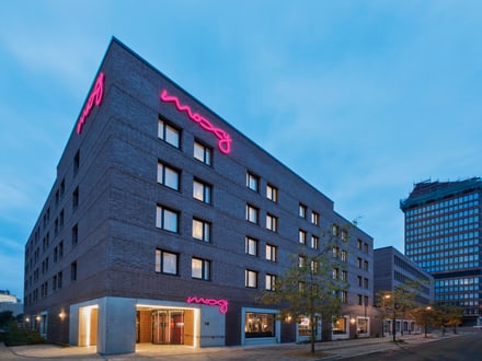 Modernes Gebäude bei Dämmerung mit neonrosa Leuchtschrift an der Fassade.