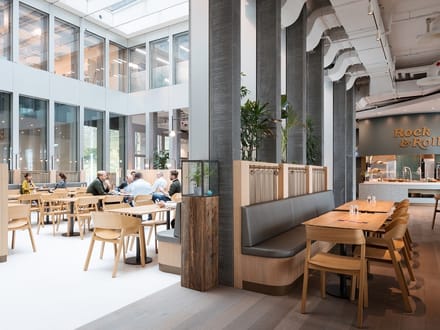 Moderne Cafeteria mit Holzmöbeln und Menschen, die an Tischen sitzen.
