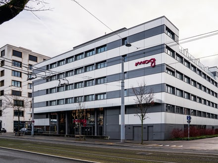 Modernes mehrstöckiges Gebäude mit Glasfassade und rotem Schriftzug.