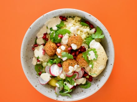 Salatschüssel mit Falafel, Couscous, Radieschen und Blattgrün auf orangem Hintergrund.