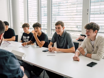 Gruppe von Jugendlichen sitzt an einem Tisch und lächelt während eines Gesprächs.