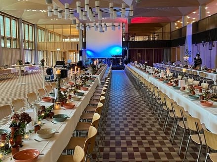 Grosser Bankettsaal mit langen, gedeckten Tischen.