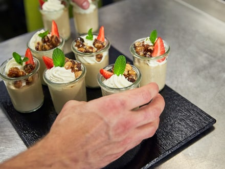 Hand arrangiert Dessertgläser mit Schlagsahne und Erdbeeren auf einem Serviertablett.