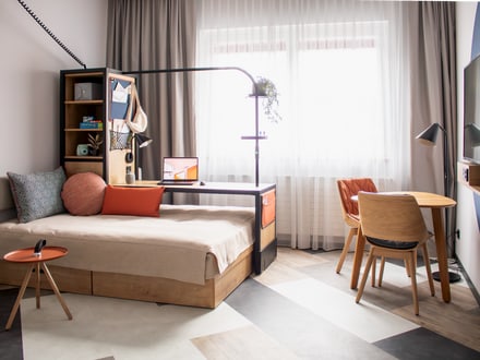 Modern eingerichtetes Hotelzimmer mit Bett, Schreibtisch und hellem Fenster.