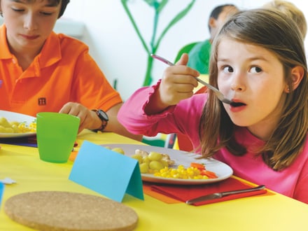 Kinder sitzen beim Mittagstisch zusammen und geniessen ihr gesundes und ausgewogenes Essen gemeinsam.