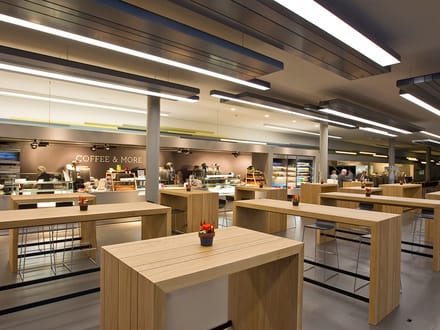 Moderne Cafeteria mit Holzstehtischen und wenigen Menschen.