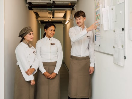 Drei Mitarbeitende in Uniformen sehen auf ein Whiteboard im Flur.