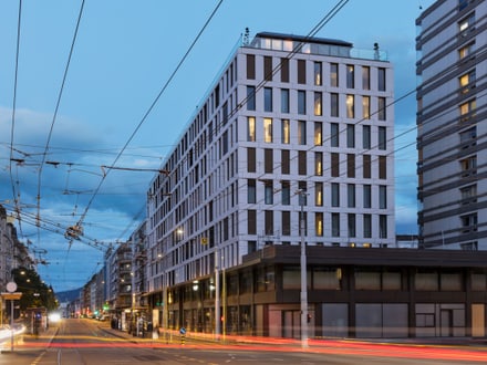 Strassenansicht mit modernen Gebäuden und Verkehrslichtern bei Dämmerung.