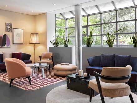 Moderne Lounge mit Sesseln, Teppichen und Pflanzen vor Fensterwand.