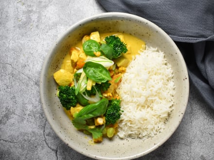 Teller mit Curry, Brokkoli und Reis auf grauem Untergrund.