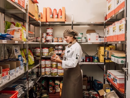 Person in Küchenkleidung, die in Vorratskammer ein Produkt ansieht.