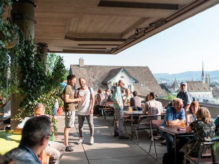Gäste geniessen ihre Getränke auf der sonnigen Terrasse der ETH mit Blick über Zürich.