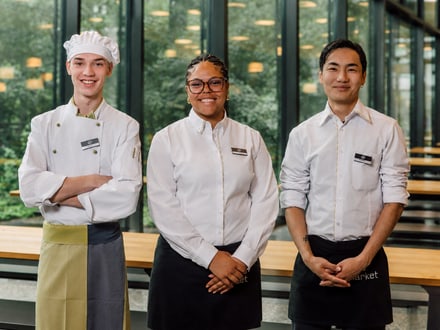 Drei Personen in Restaurantuniform stehen in einem Innenraum.
