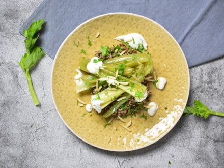 Gourmetgericht mit grünem Gemüse und Sauce auf einem gelben Teller.