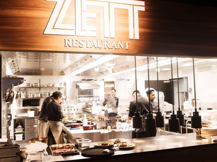 Blick in die offene Küche des ZLETT Restaurants mit arbeitenden Köchen.