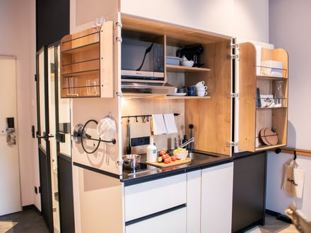 Kompakte Kücheneinheit in einem modernen Apartment mit offenen Schränken und Küchenutensilien.
