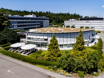 Luftaufnahme eines Bürogebäudes mit Terrassenbereich und Bäumen.