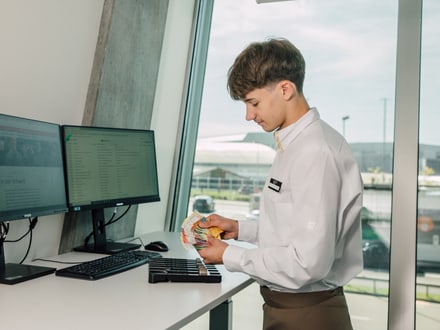 Person in weissem Hemd zählt Karten vor Computermonitoren.