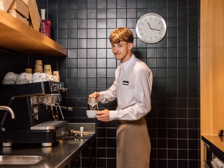 Mann in weissem Hemd, der an einer Espressomaschine in einer modernen Küche arbeitet.