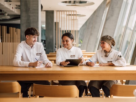 Drei Restaurantmitarbeiter in Uniform am Tisch sitzend, lächelnd.