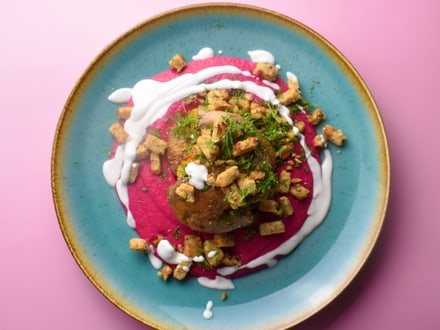 Gourmetgericht auf blauem Teller mit rosa Hintergrund.