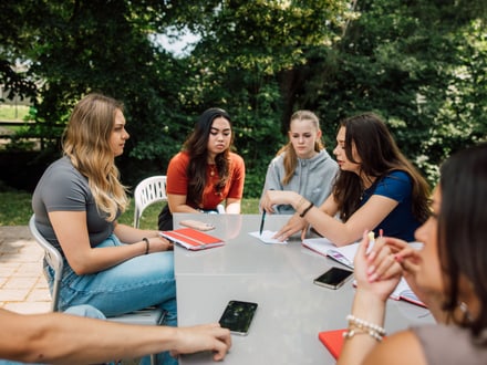Eine Gruppe von Frauen sitzt draussen an einem Tisch und spricht.
