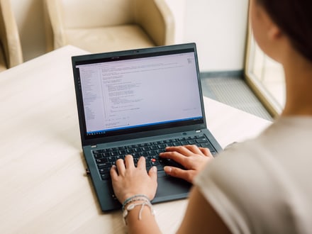 Person bei der Arbeit an einem Laptop mit Programmiercode auf dem Bildschirm.